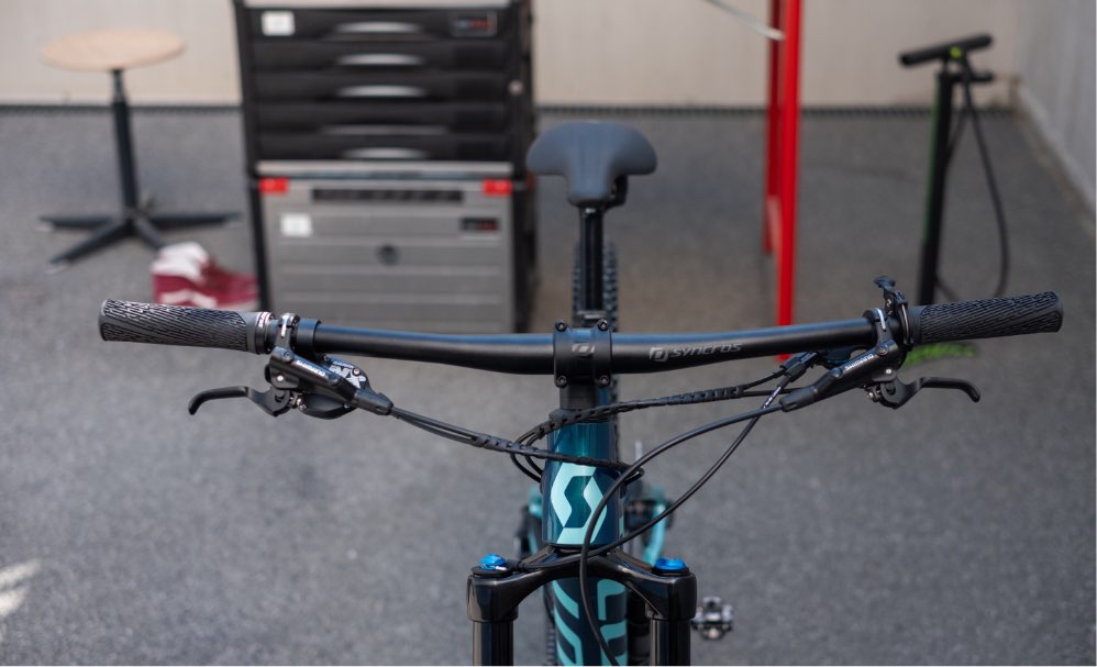 Der lenker eines mountainbikes in der werkstatt auf schwarzem hintergrund  austausch des schaltseils im fahrrad der mechaniker hält ein neues seil in  der hand