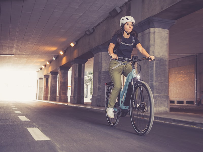femme portant un casque blanc, sur un vélo électrique bleu, dans un tunnel