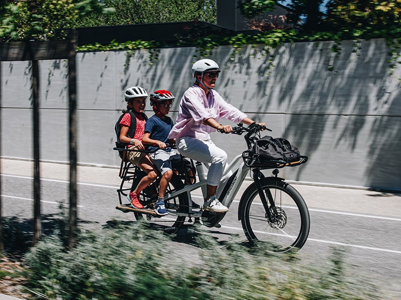 un adulte et 2 enfants sur un vélo cargo blanc