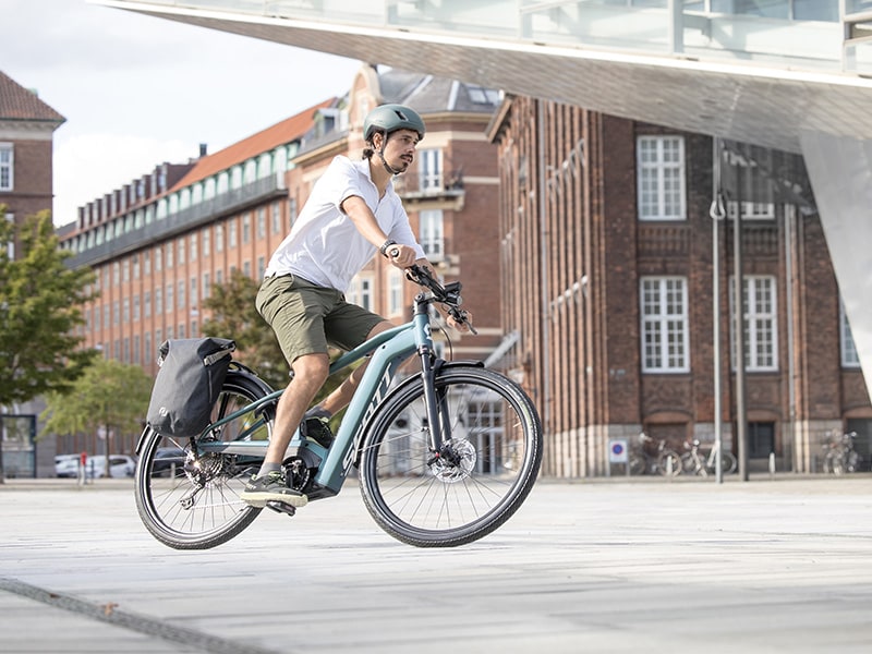 un homme sur un vélo électrique bleu équipé de pare-boues et de sacoches