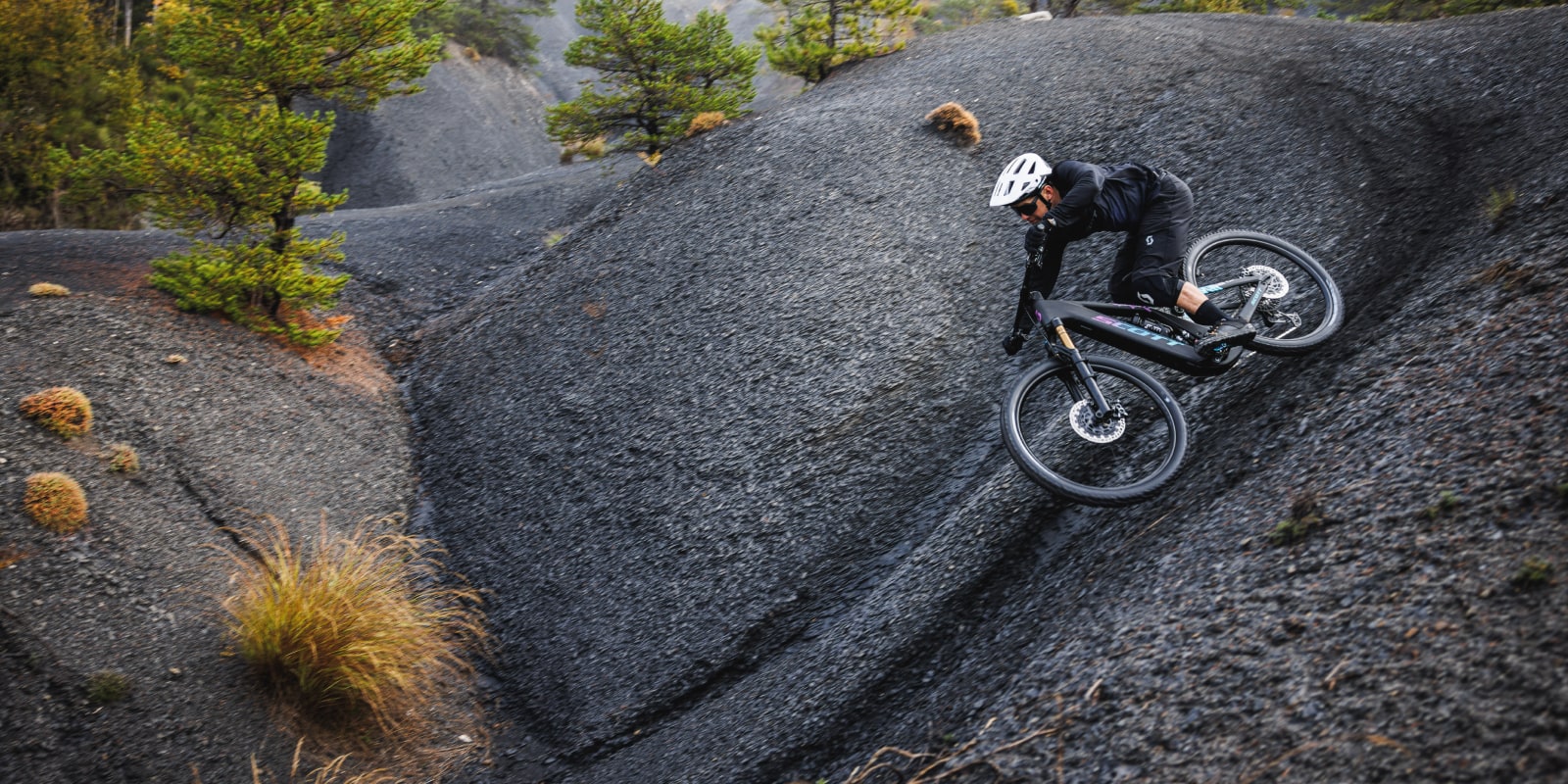 guy on a black patron, with a white helmet, doing turns on black rocks, going left