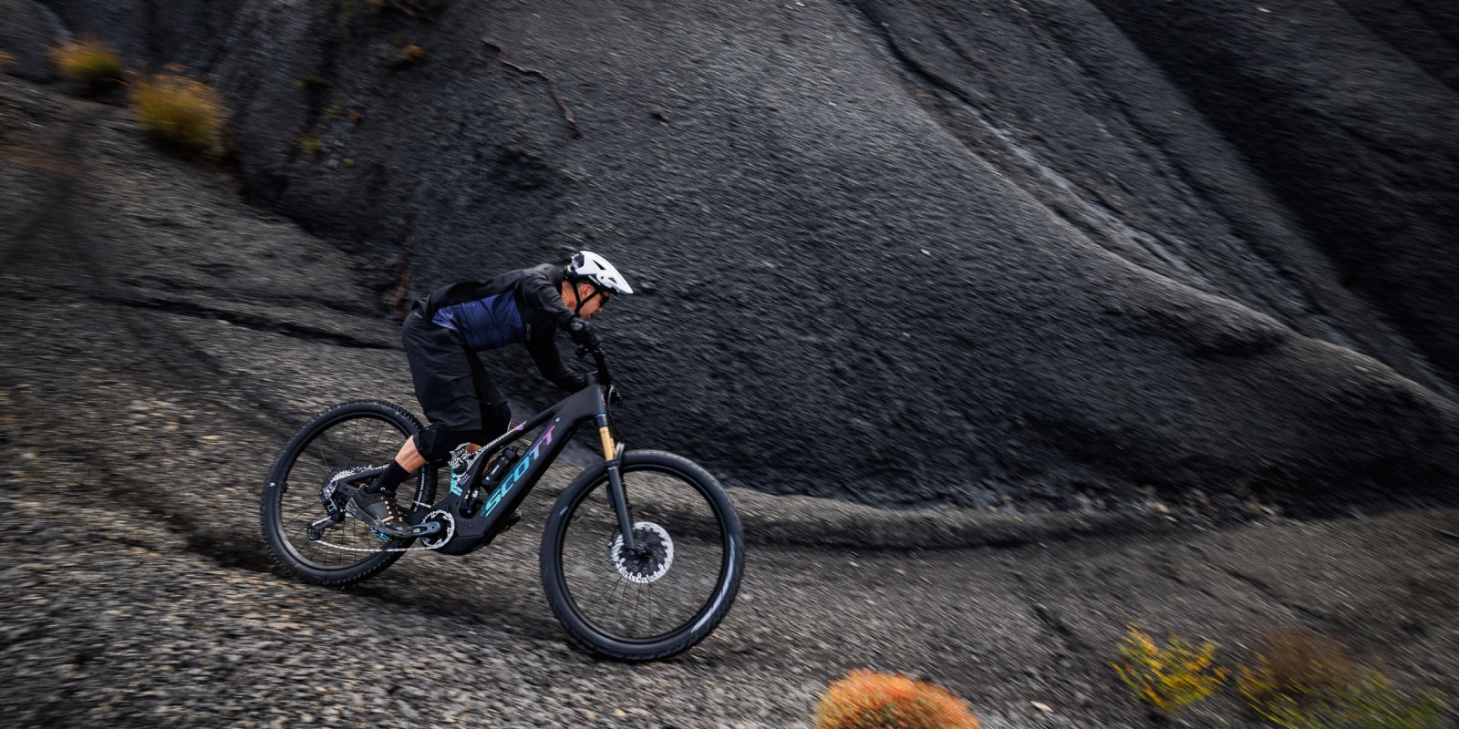 guy on a black patron, with a white helmet, doing turns on black rocks, going right