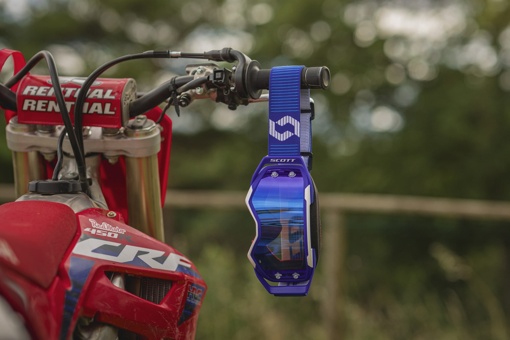 blue goggle with a blue chrome screen hanging to a red motorbike handlebar