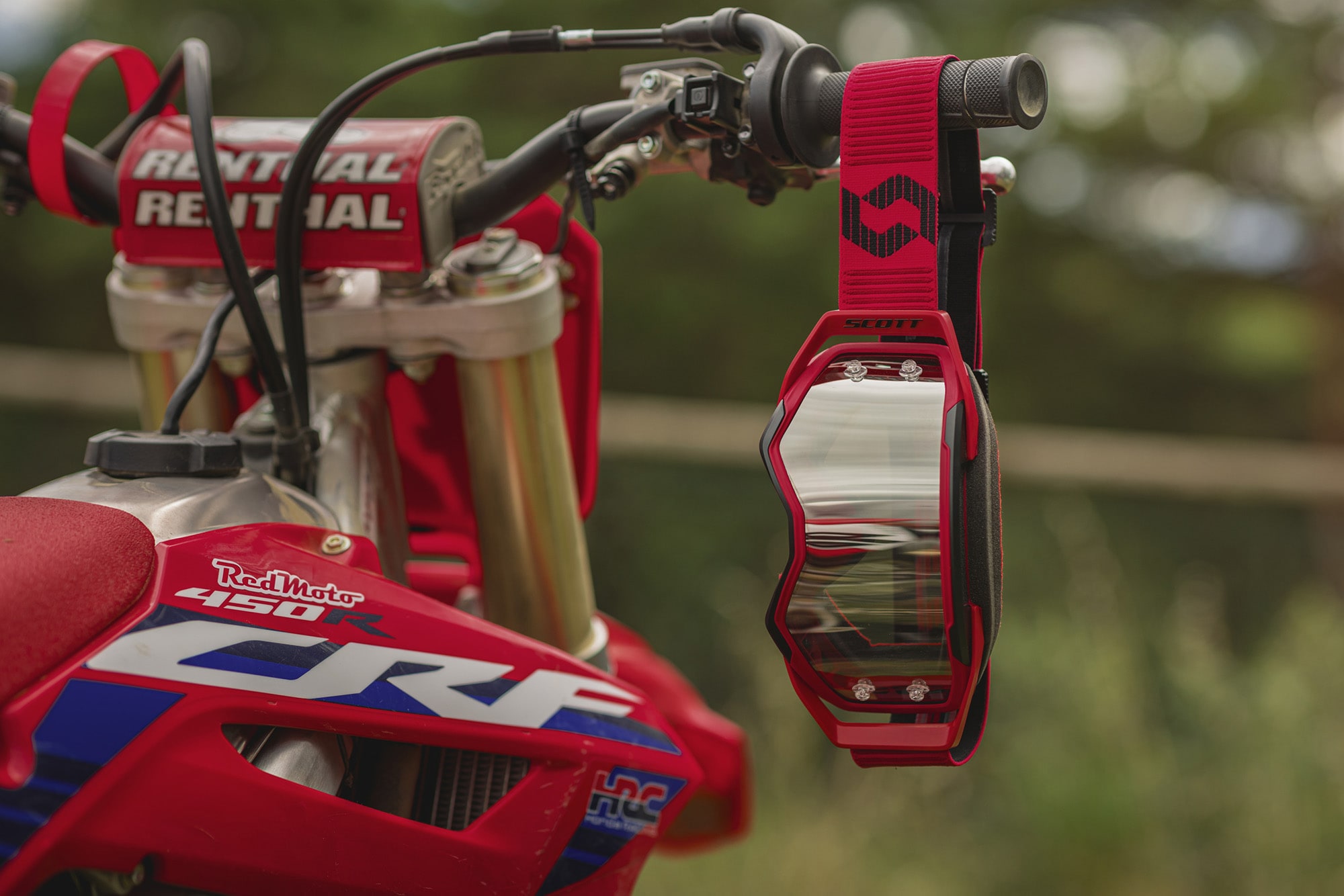 red goggle with a grey screen hanging to a red motorbike handlebar