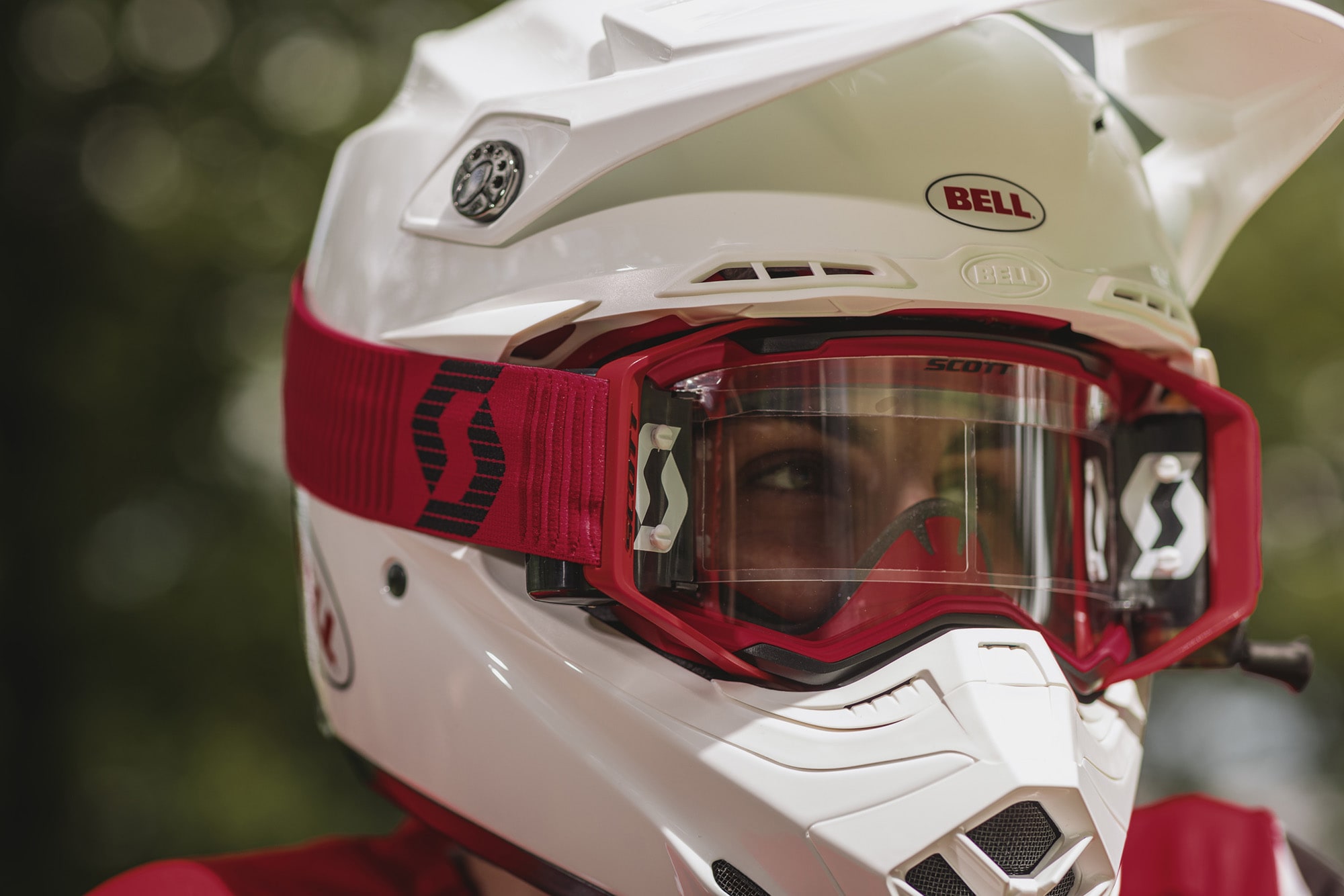 close-up shot of a rider wearing a red and black goggle with a clear screen and a white helmet