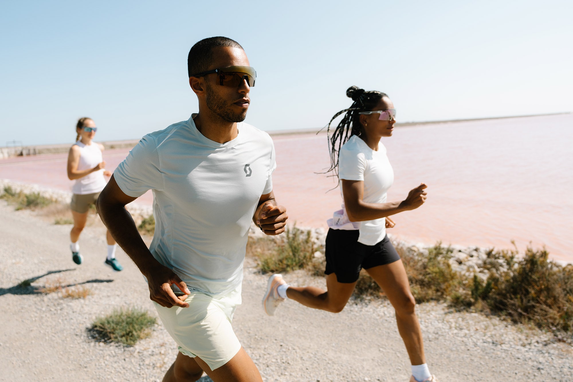 Side view of three runners moving through a lush forest trail in SCOTT Sports gear and Pursuit Gravel running shoes, representing the essence of outdoor running experience.